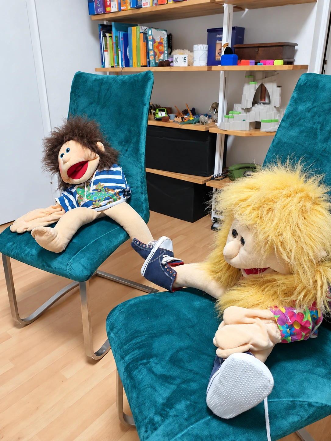 Hand puppets on turquoise chairs beside shelves of play materials