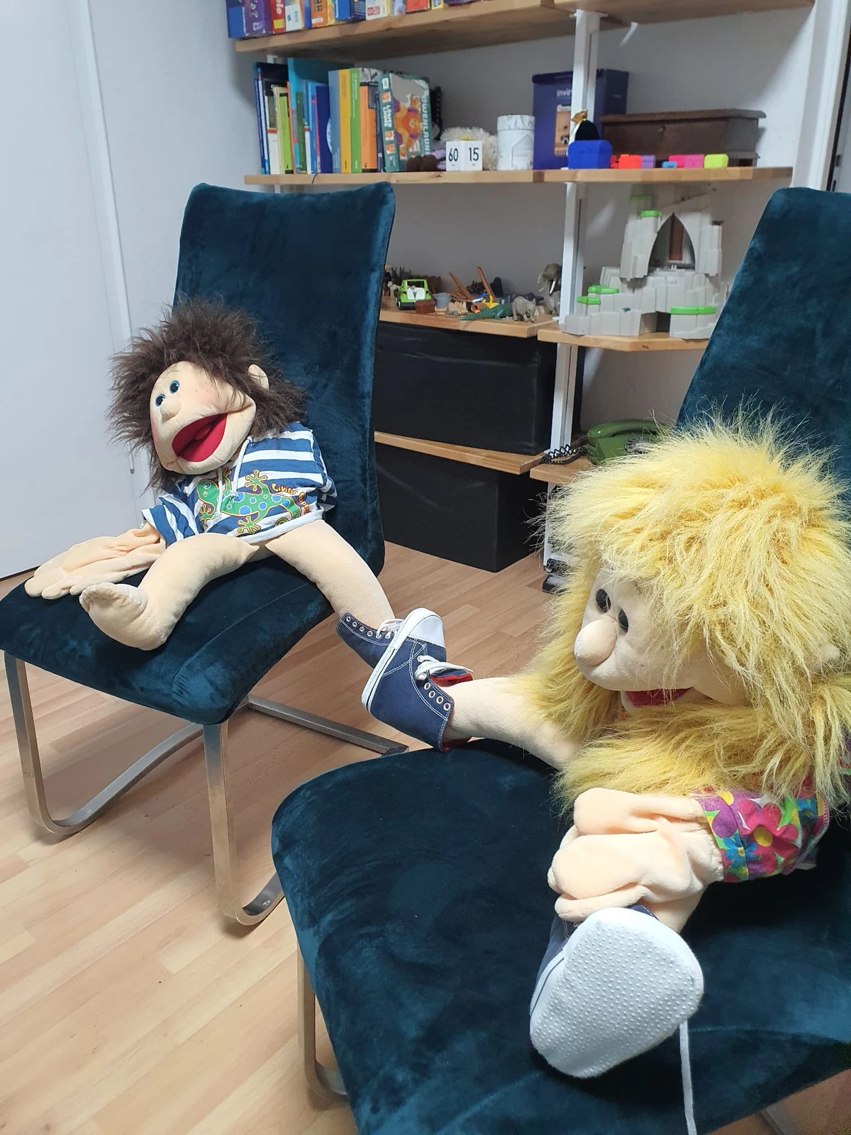 Marionnettes sur des fauteuils bleus devant des étagères de jeux