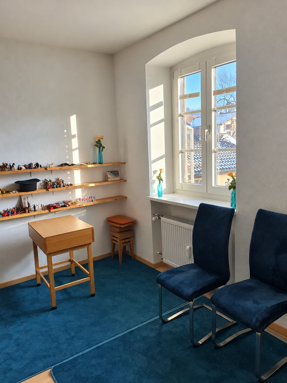 Salle d’échange avec deux fauteuils bleus, une table en bois et des étagères de jouets près de la fenêtre
