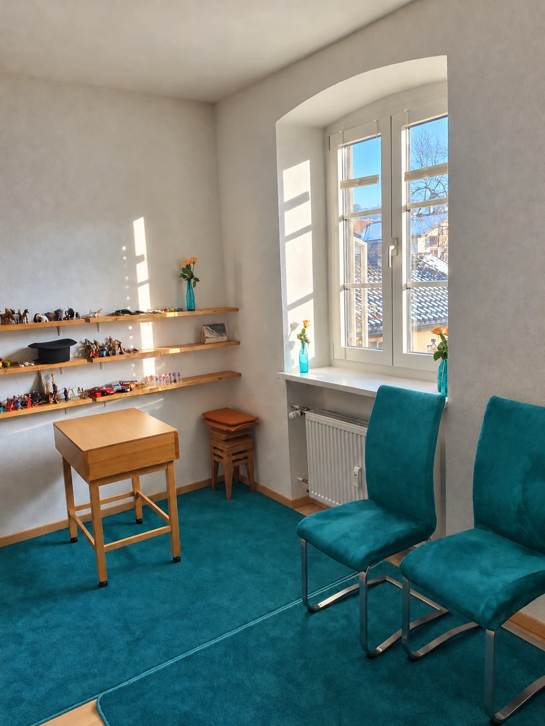 Conversation room with two turquoise chairs, a wooden table and toy shelves beside the window